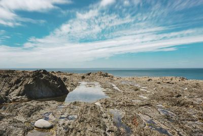 Scenic view of rocky coastline and sea against cloudy sky