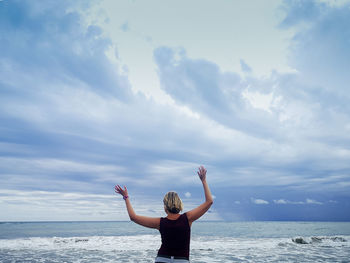 Rear view of woman standing in sea against sky