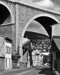 Bridge over road by buildings in city against sky