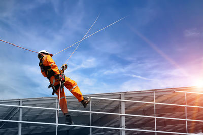 Low angle view of man working on rope against sky