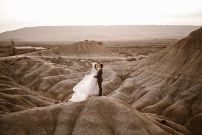 High angle of groom and bride embracing near mountain against cloudy sundown sky in bardenas reales natural park in navarra, spain