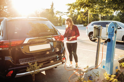 Woman charging black electric car at station on sunny day