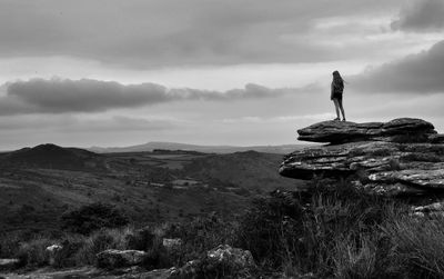 Person standing on rock looking at mountain against sky