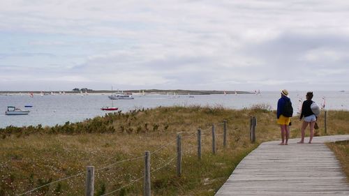 Rear view of women walking on beach against sky