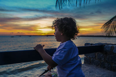 Side view of boy standing on beach against sky during sunset