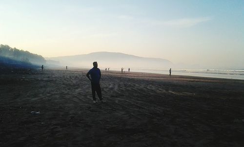 Rear view of silhouette man standing on beach against sky