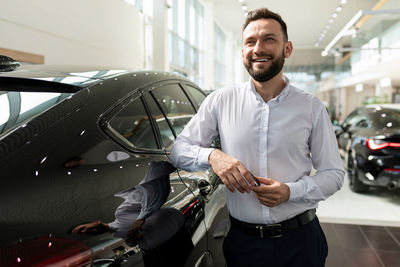 Happy man leaning on car in showroom