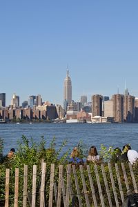 View of cityscape by sea against clear blue sky