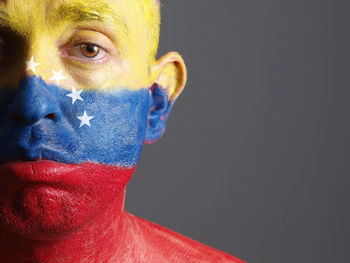 Close-up portrait of sad man with venezuelan flag body paint against gray background