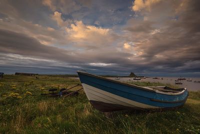 Boats moored on field against sky during sunset