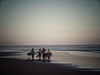 Surfers discussing while standing at sea shore against clear sky