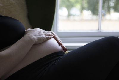 Midsection of woman sitting by window at home