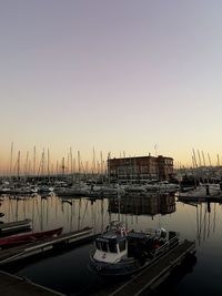 Sailboats moored in harbor at sunset