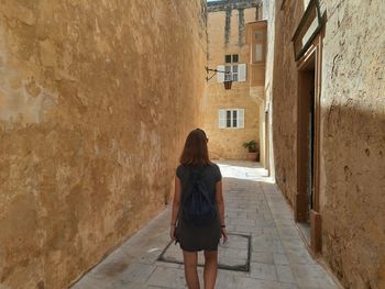 Rear view of woman walking on footpath amidst buildings in city