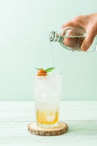 Cropped hand pouring water in glass against white background