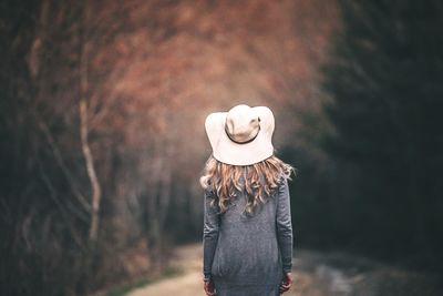 Rear view of woman wearing hat and long coat at park during autumn