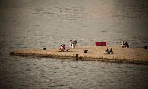 Mid distant view of people relaxing at harbor by sea