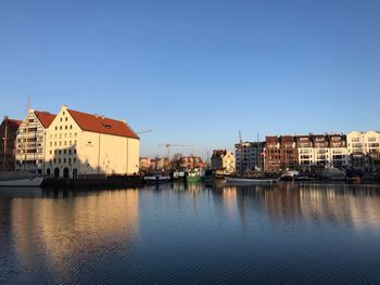 Buildings by river against clear blue sky