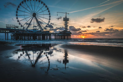 Silhouette ferris wheel by sea against sky at sunset