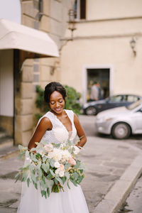 Smiling bride holding bouquet while standing on road