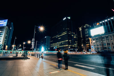 People on illuminated city street and buildings at night