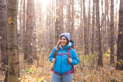 Smiling woman standing by tree trunk in forest during winter