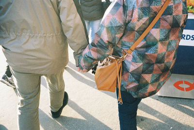 Low section of two people walking outdoors holding hands