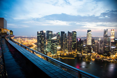 Illuminated buildings by river against sky in city