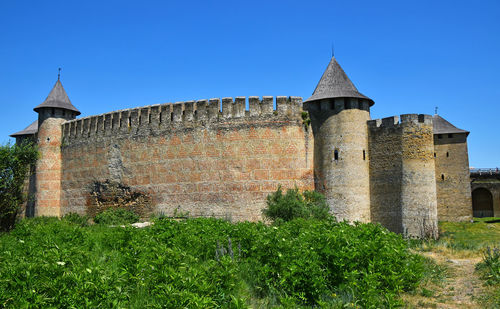 Khotyn fortress by grassy field against clear blue sky