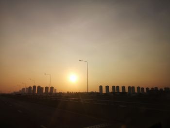 City street and silhouette buildings against sky during sunset