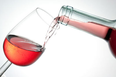 Close-up of wine pouring from bottle in glass against white background