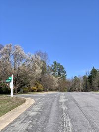 Road amidst trees against clear blue sky