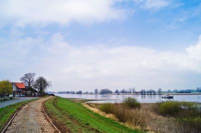 Footpath by lake against sky