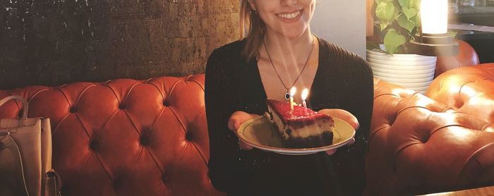 Midsection of woman holding plate with cake while sitting on sofa at home