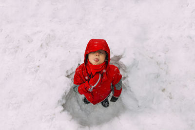 High angle view of playful boy catching snowflakes on tongue while standing in snow