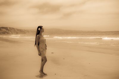 Beautiful young woman standing at beach against sky