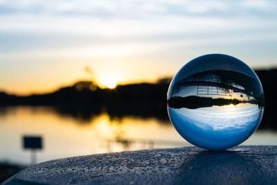 Close-up of crystal ball on lake against sky during sunset