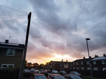 Cars on road by buildings against sky at sunset