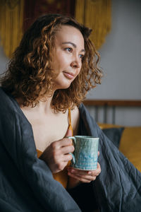 Beautiful lady in a blanket on the bed and holding morning coffee