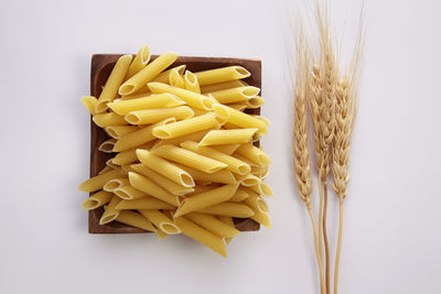 Close-up of pasta in bowl by wheat against white background
