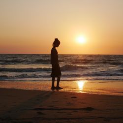 Silhouette woman walking at beach during sunset