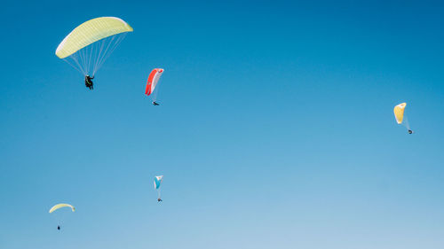 Low angle view of paragliding against clear blue sky