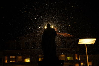 Rear view of silhouette man standing against illuminated city at night