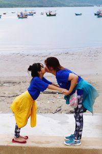 Side view of mother kissing daughter on mouth at beach