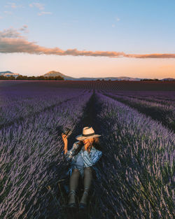 Full length of woman sitting on flowering field against sky