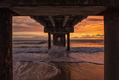 Waves on shore under pier during sunset