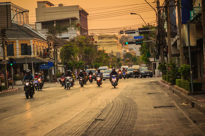 People on street amidst buildings in city at sunset