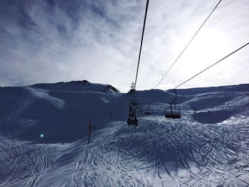 Overhead cable car over snowy mountains against cloudy sky on sunny day