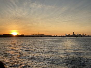 Silhouette buildings by sea against sky during sunset