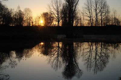 Silhouette bare trees by lake against sky during sunset